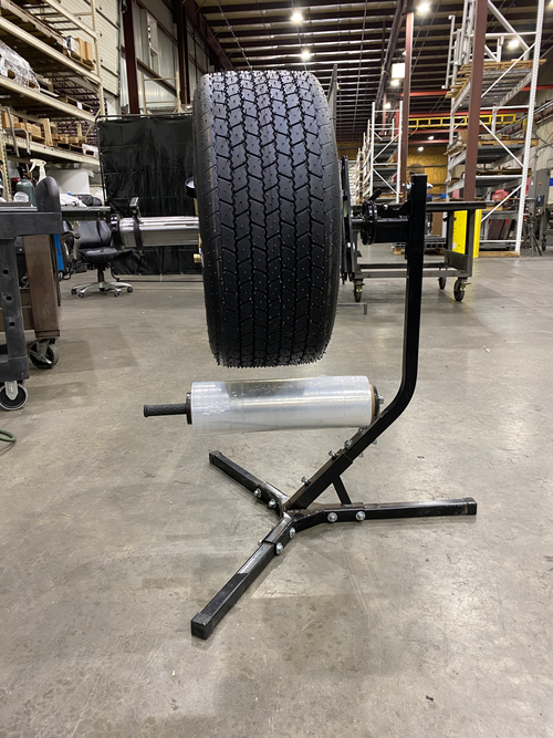 A dirt race tire is standing on an EZ manual tire prep stand in a warehouse